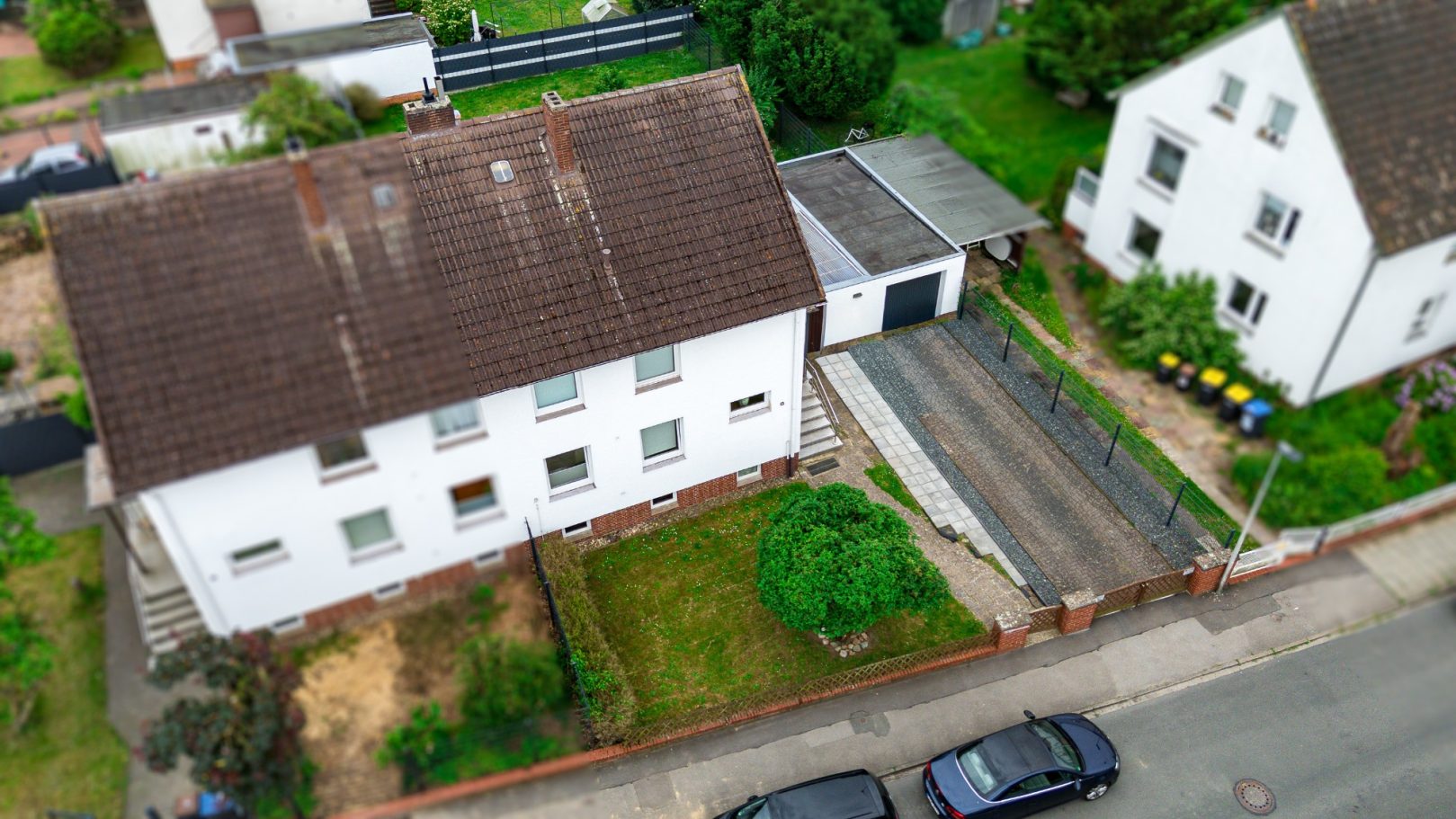 Zwei weiße Wohnhäuser mit Garagen und Fahrweg, umgeben von Grünanlagen.