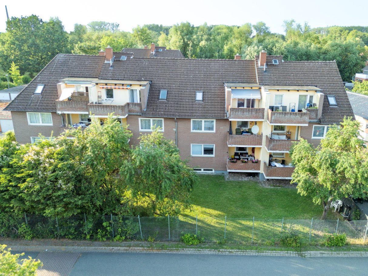 Einfamilienhaus mit Balkonen und Garten, umgeben von Bäumen und Buschwerk.